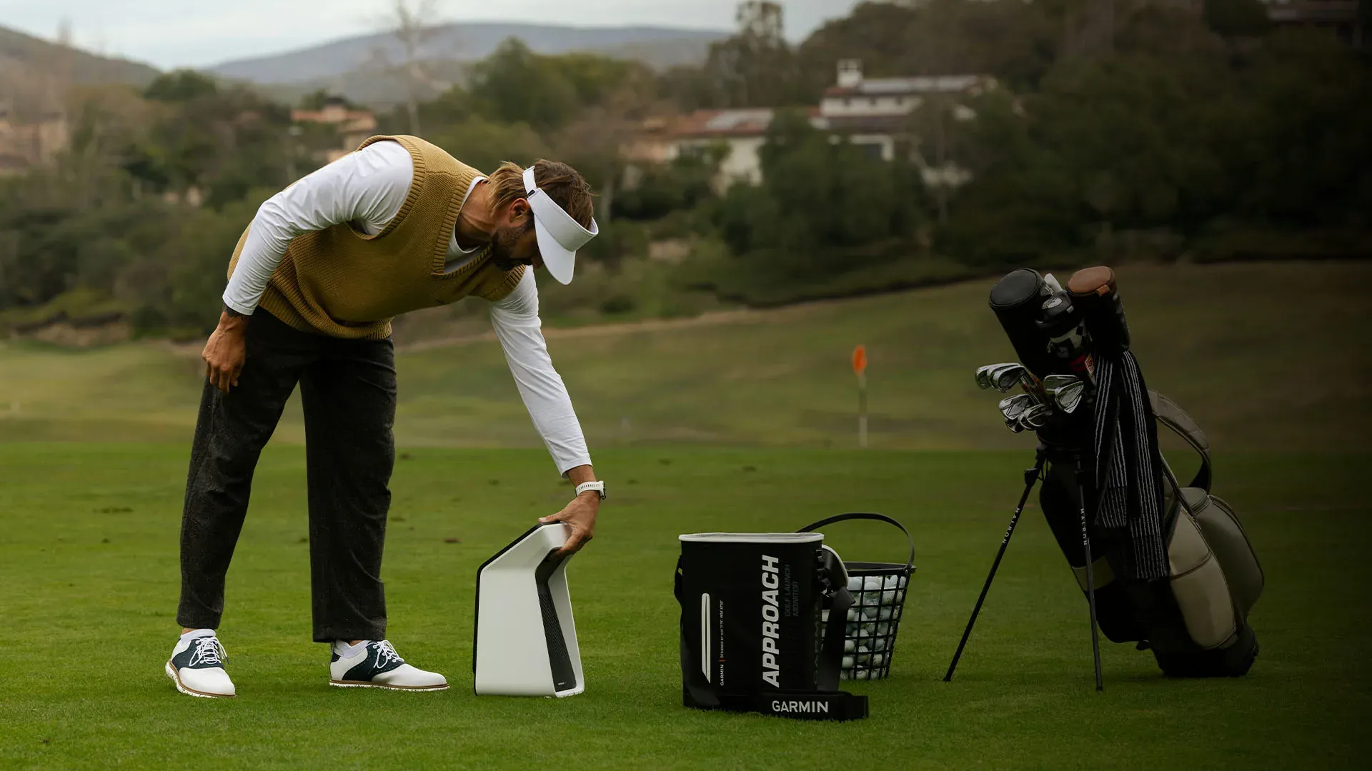 Golfer setting up the Garmin R50 on the driving range next to a golf bag and ball basket